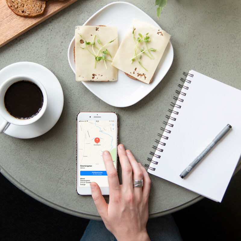 cafébord sett ovanifrån med en kopp kaffe, två smörgåsar på ett fat, en mobil och en anteckningsbok